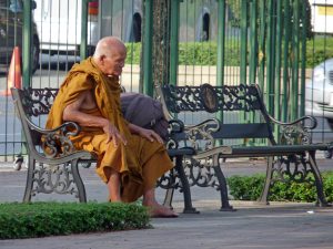 älterer Mönch nimmt sich seine Pause auf einer Parkbank in Bangkok